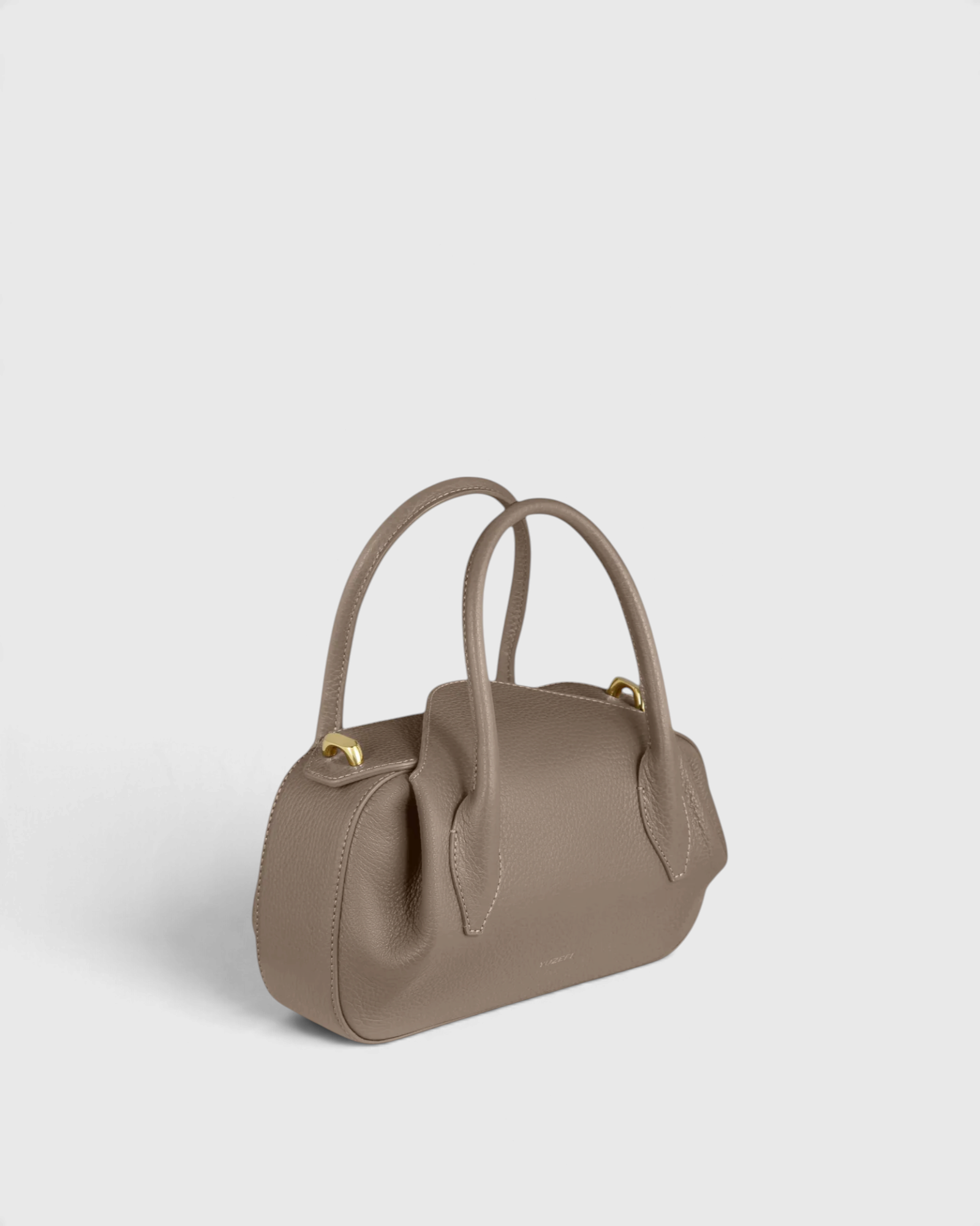 JONES + CO Oyster Mini Duffle in taupe pebble grained Italian leather with gold-tone hardware and top handles.
