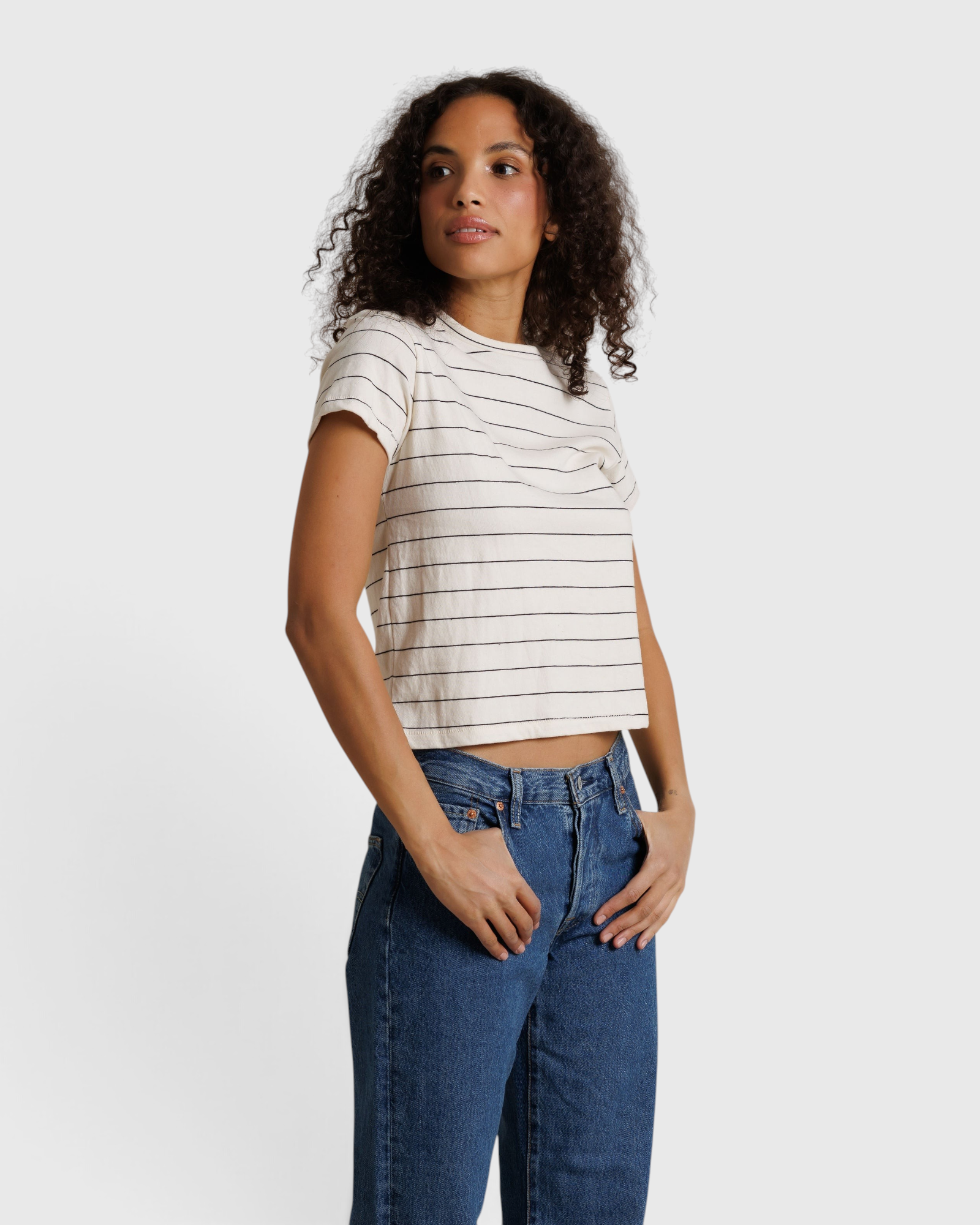 Model wearing JONES + CO Lisa Tee in natural stripe recycled cotton with a shrunken neckline and blue denim jeans.