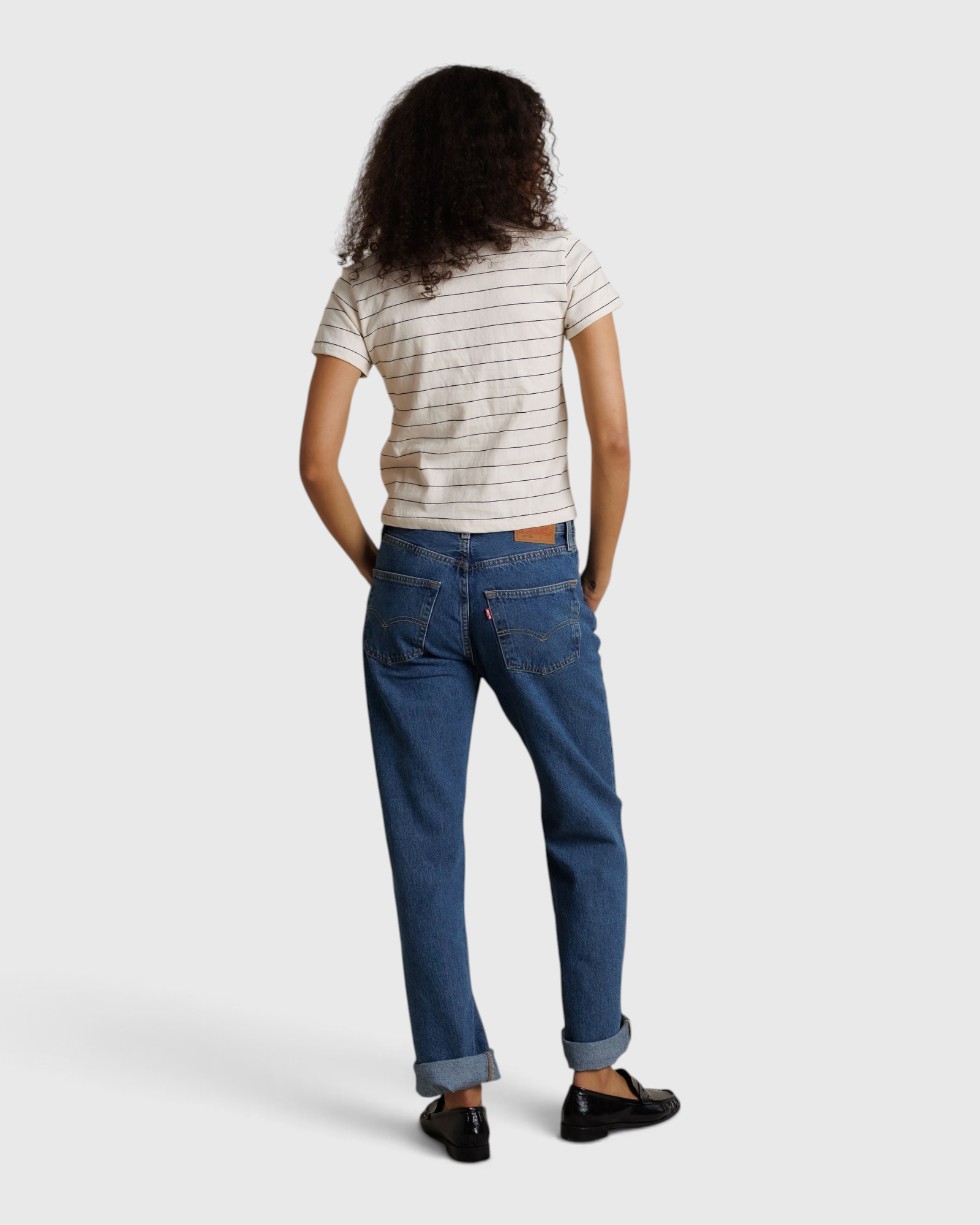 Model wearing JONES + CO Lisa Tee in natural stripe recycled cotton, paired with blue denim jeans, back view.