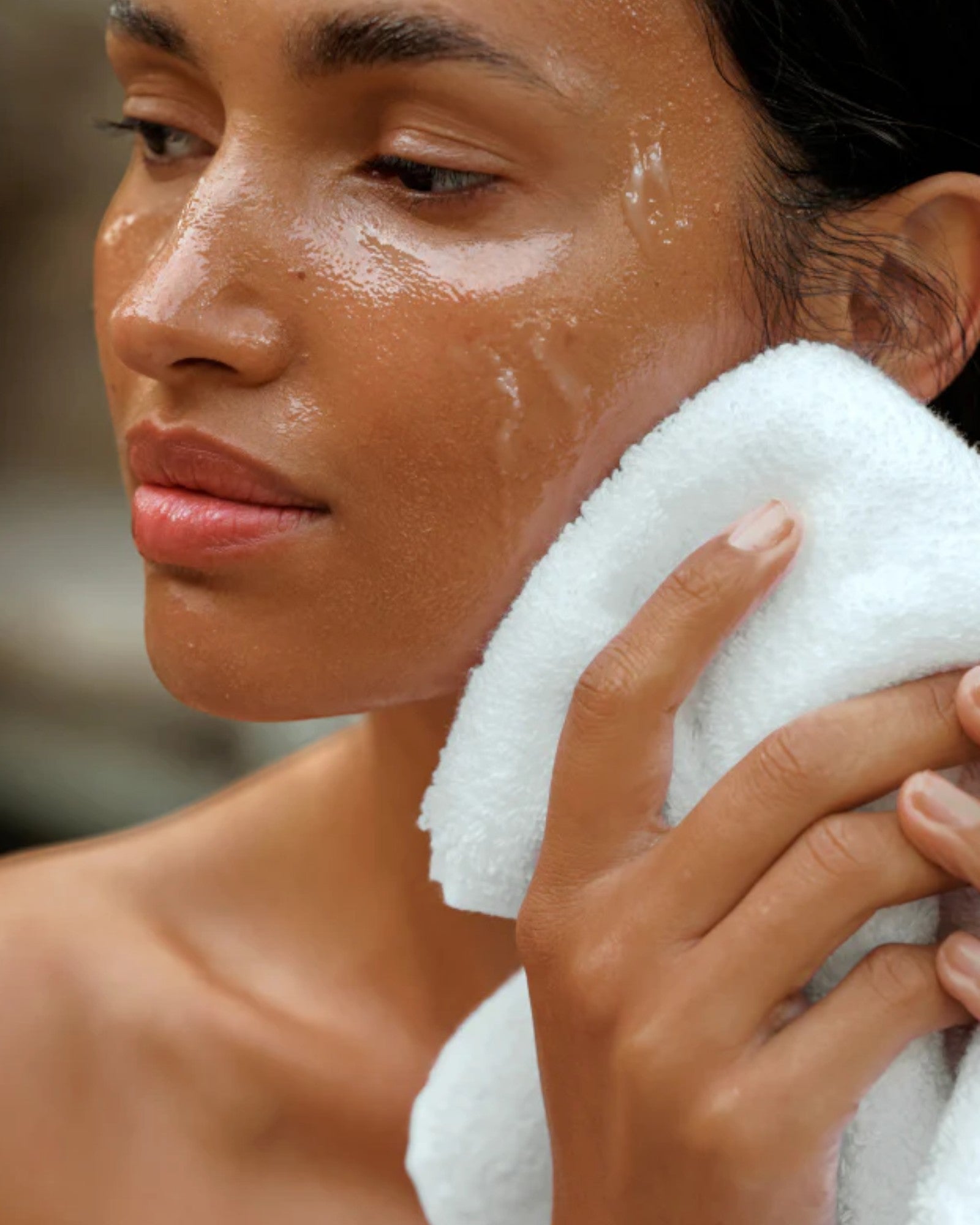 Woman holding a white towel to her face with a blurred background