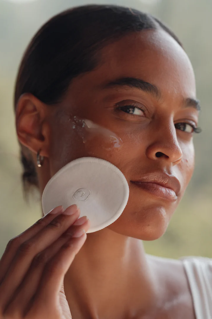 Woman applying a white round compact to her face with a blurred natural background