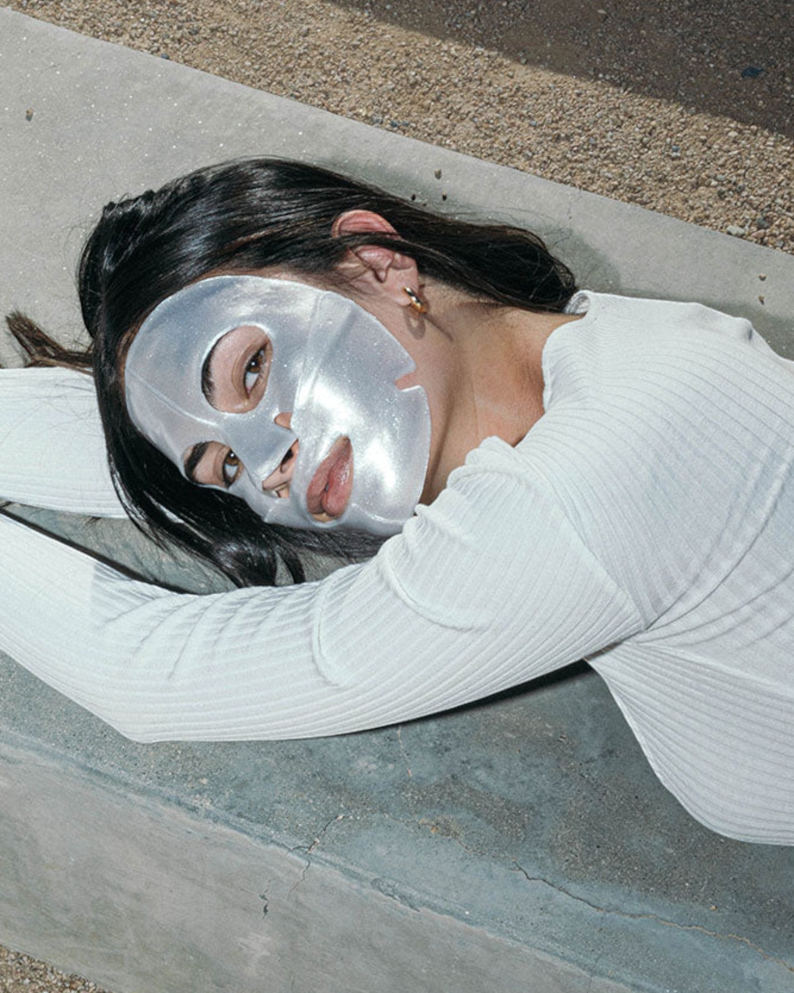 Person wearing a silver face mask lying on a concrete surface.