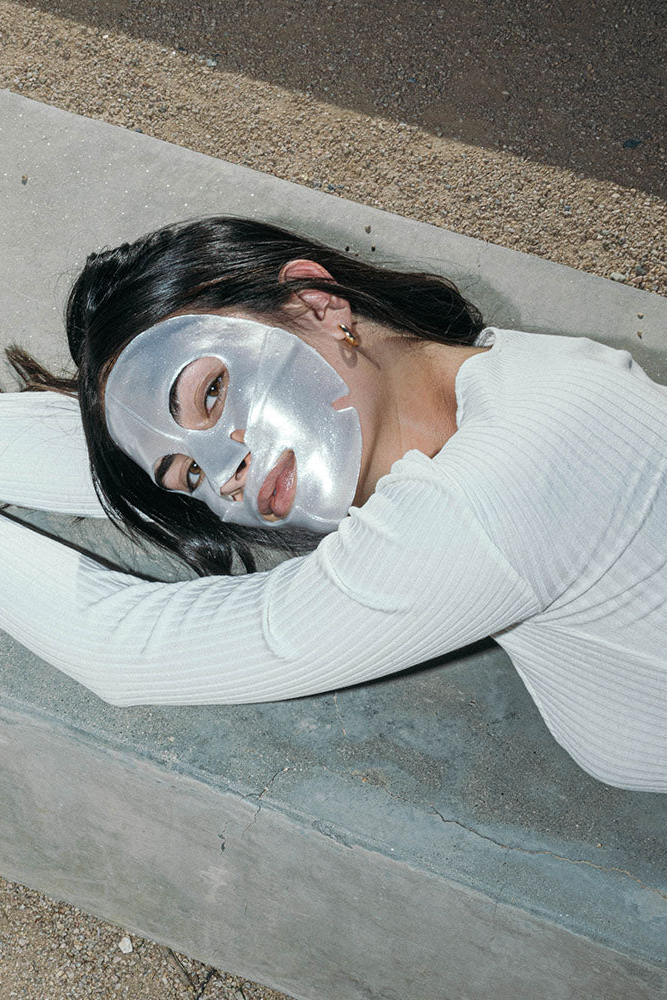 Person wearing a silver face mask lying on a concrete surface.