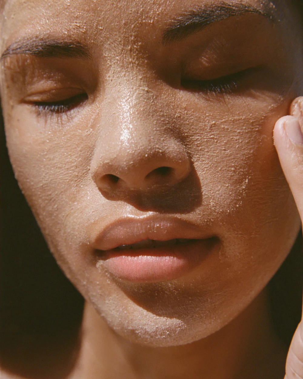 Close-up of a person's face with a sun-kissed complexion and mud mask on skin