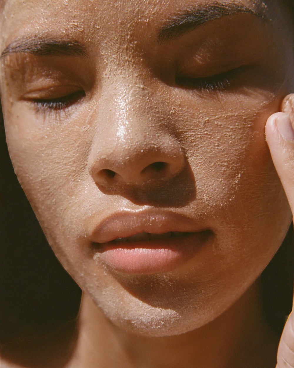 Close-up of a person's face with a sun-kissed complexion and mud mask on skin
