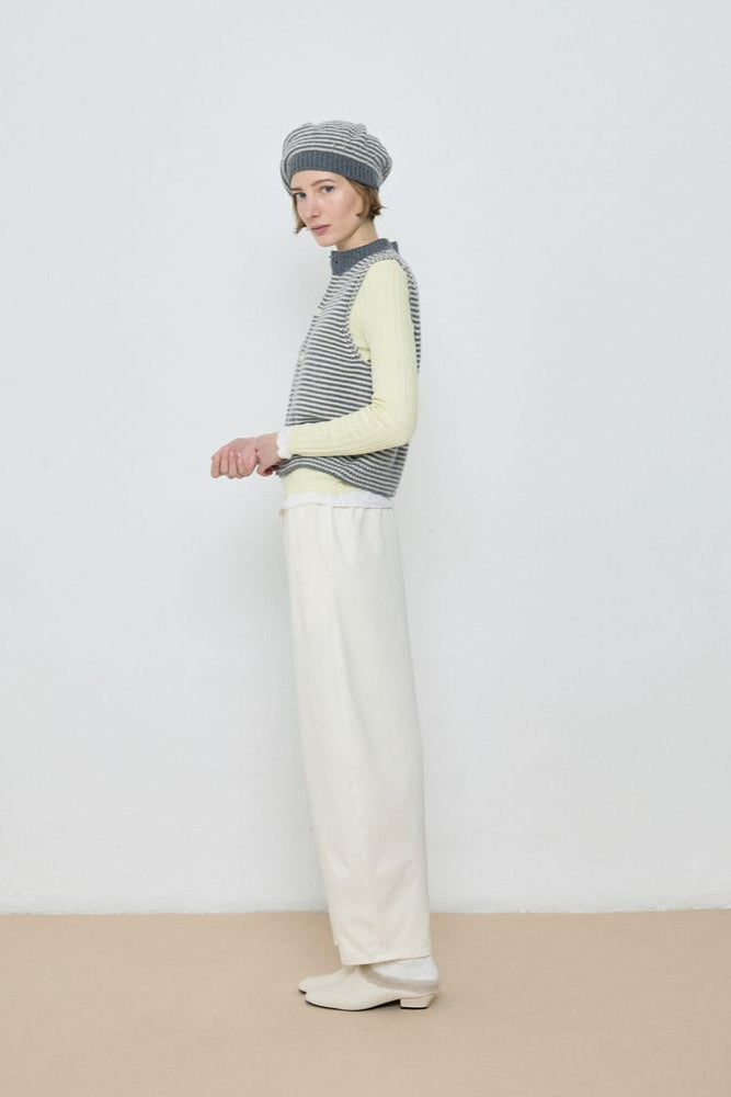 Person wearing a colorful sweater and white pants against a plain background