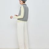 Person wearing a striped sweater vest, white pants, and a beanie against a plain background