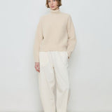 Person wearing a beige sweater and white pants against a plain background