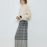 Person wearing a cream sweater and plaid skirt against a white background