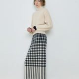 Person wearing a cream sweater and plaid skirt against a white background