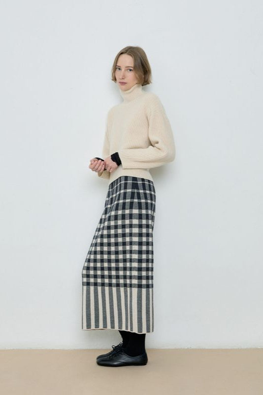 Person wearing a cream sweater and plaid skirt against a white background