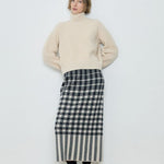 Woman wearing a beige sweater and black and white checkered skirt against a plain background