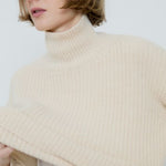 Woman wearing a beige turtleneck sweater against a white background