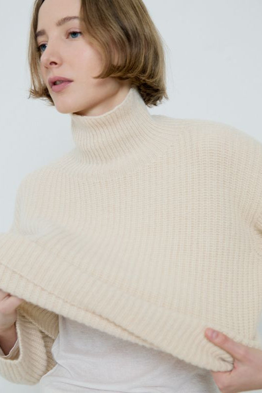 Woman wearing a beige turtleneck sweater against a white background