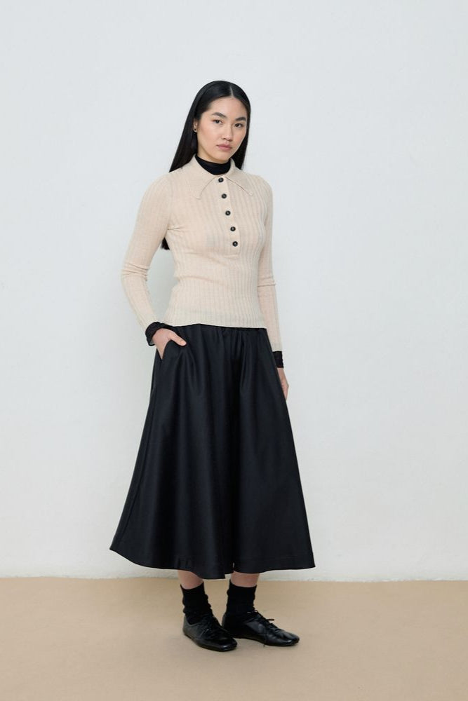 Person wearing a beige sweater and black skirt against a white background