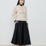 Person wearing a beige sweater and black skirt against a white background