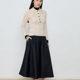 Person wearing a beige sweater and black skirt against a white background