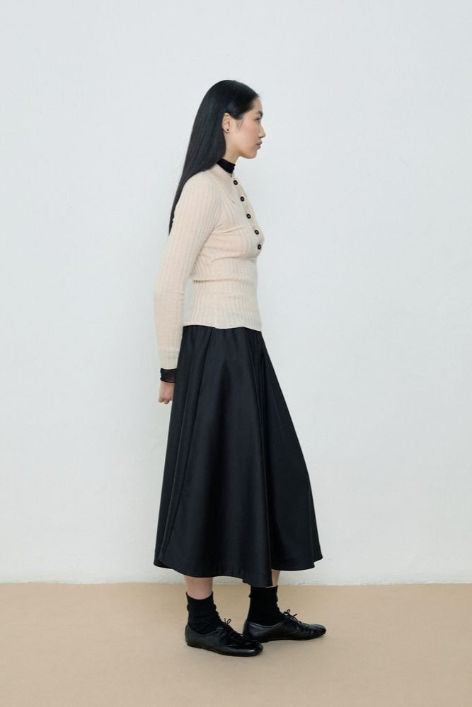 Woman wearing a beige sweater and black skirt against a white background