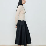 Woman wearing a beige sweater and black skirt against a white background