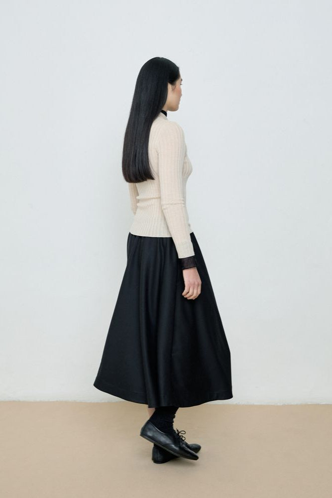 Person wearing a black skirt and cream sweater against a white background