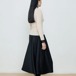 Person wearing a black skirt and cream sweater against a white background