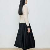 Person wearing a black skirt and cream sweater against a white background