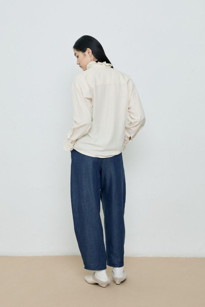 Person wearing a white blouse and blue pants against a plain background