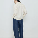Person wearing a white blouse and blue pants against a plain background