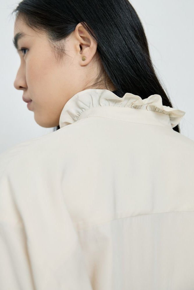 Person wearing a light-colored shirt with a plain background