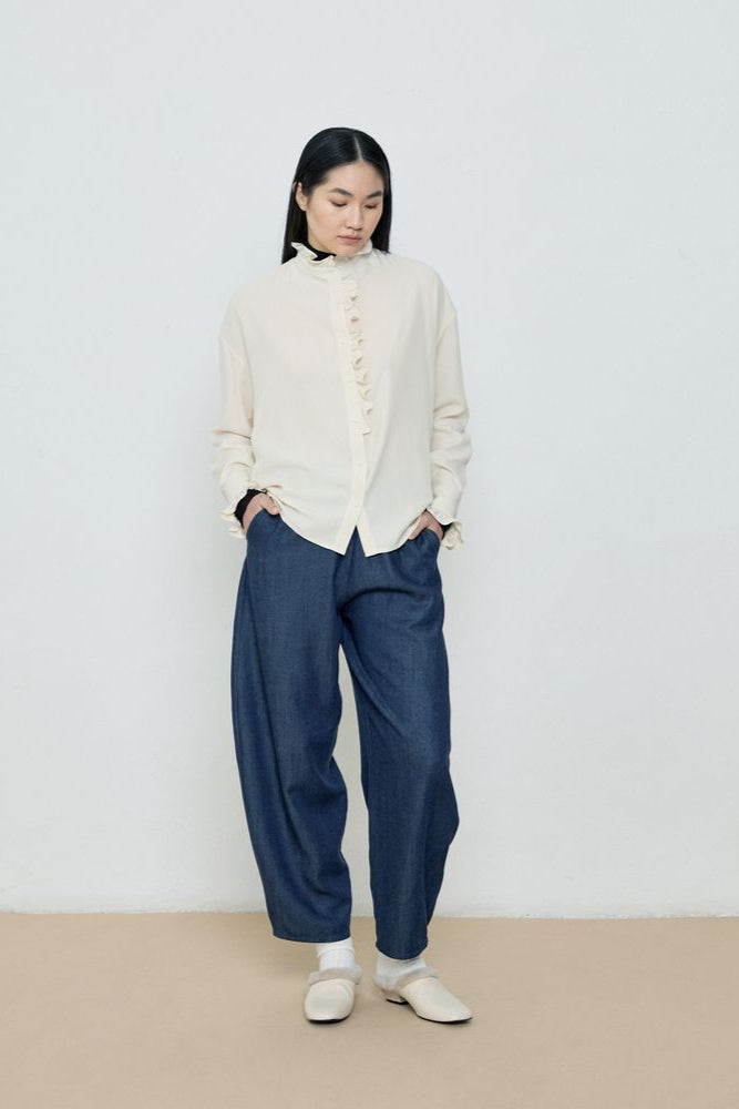 Person wearing a white blouse and blue pants against a plain background