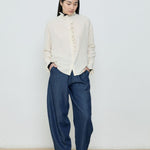 Person wearing a white blouse and blue pants against a plain background