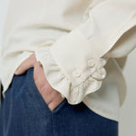 Person wearing a white blouse with ruffled cuffs and blue pants on a plain background