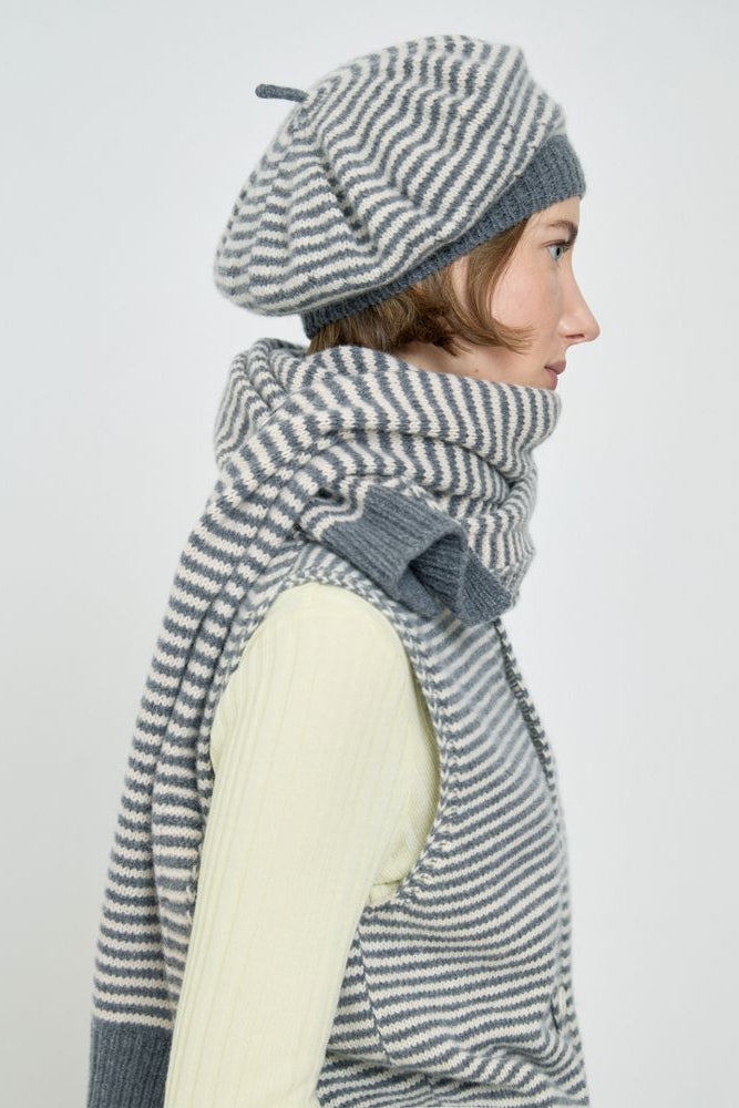 Woman wearing a gray and white striped scarf and beret on a light background