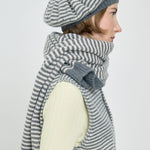 Woman wearing a gray and white striped scarf and beret on a light background