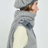 Woman wearing a gray and white striped scarf and beret on a light background