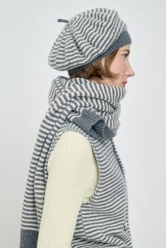 Woman wearing a gray and white striped scarf and beret on a light background