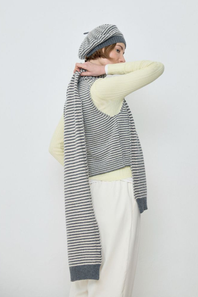 Person wearing a striped sweater, white pants, and a gray beanie on a plain background