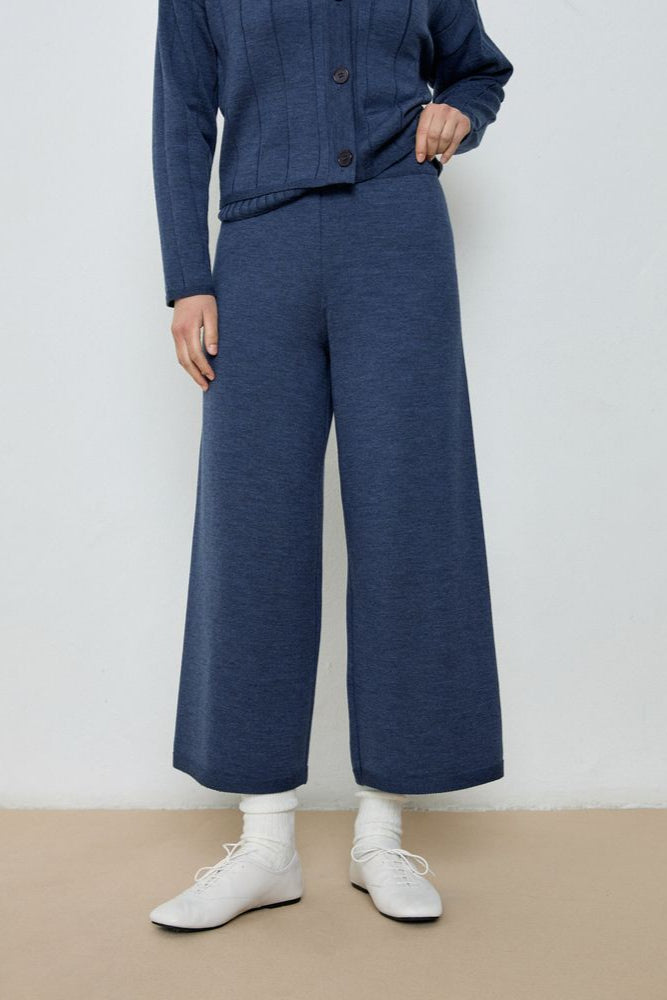 Person wearing a blue outfit with wide-leg pants and white shoes on a plain background