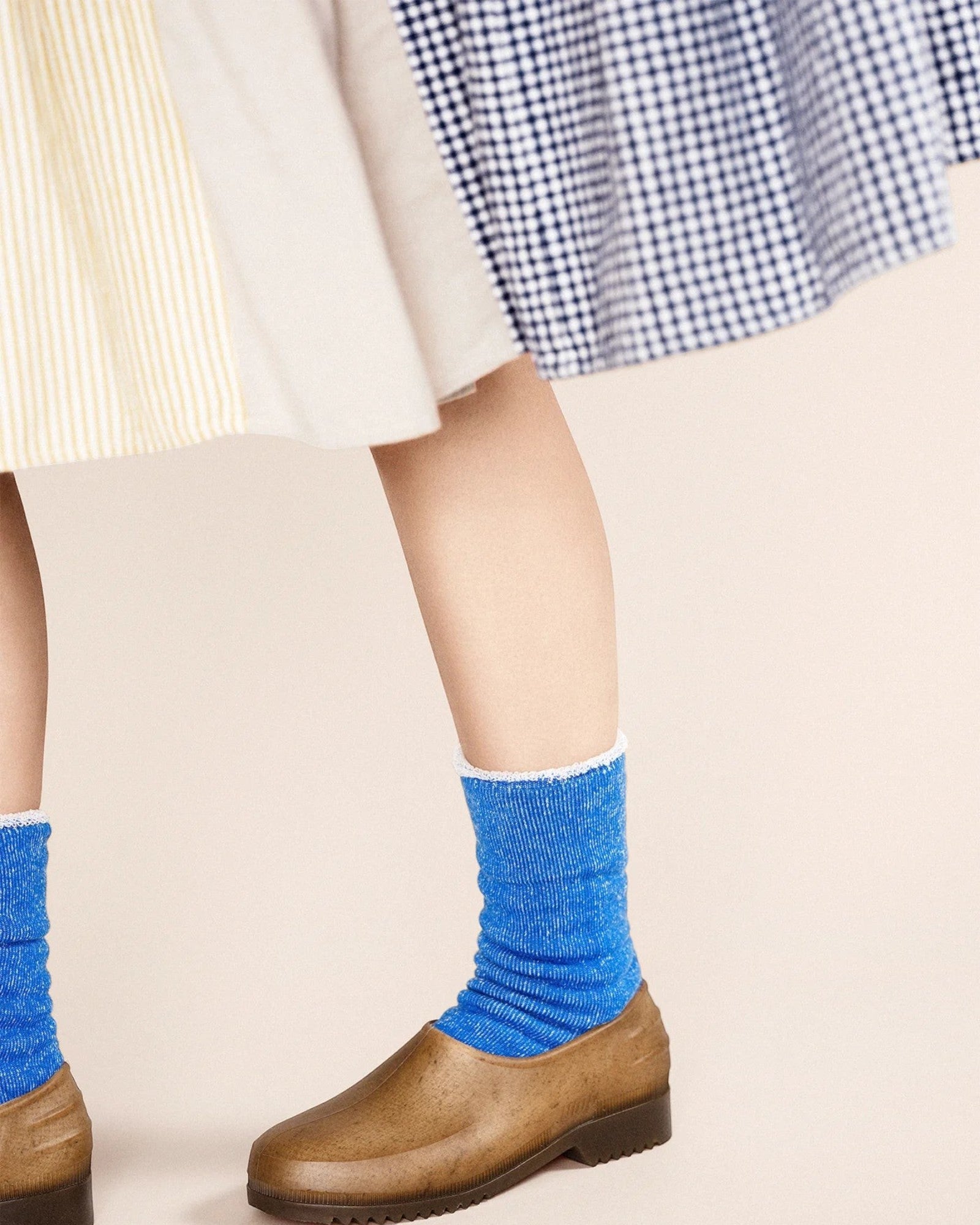 Person wearing blue socks and brown shoes on a beige background