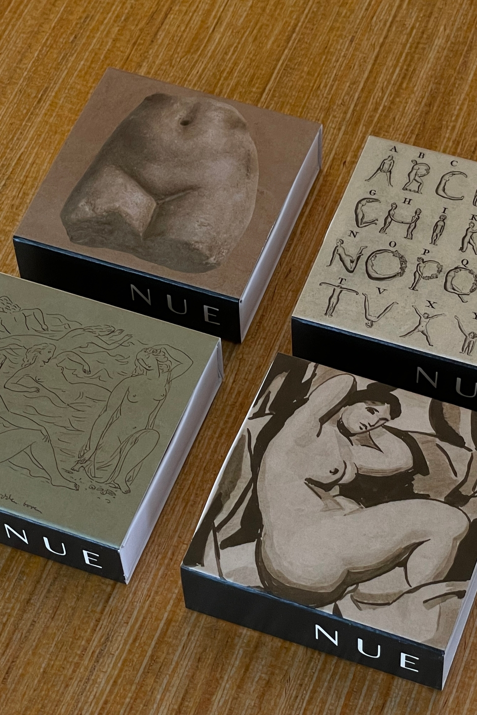 Four boxes with artistic designs and 'NUE' branding on a wooden surface