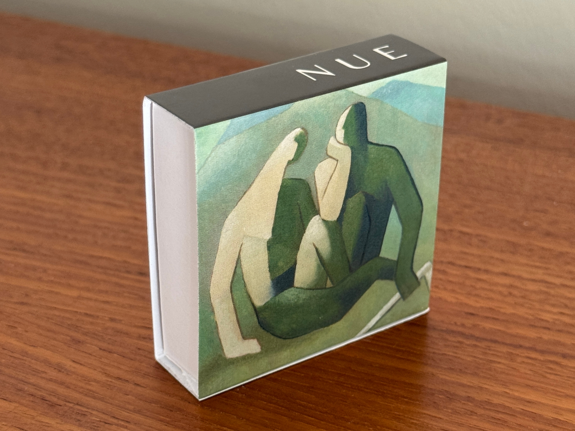 Product packaging with abstract art design and 'NUE' branding on a wooden surface