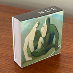 Product packaging with abstract art design and 'NUE' branding on a wooden surface