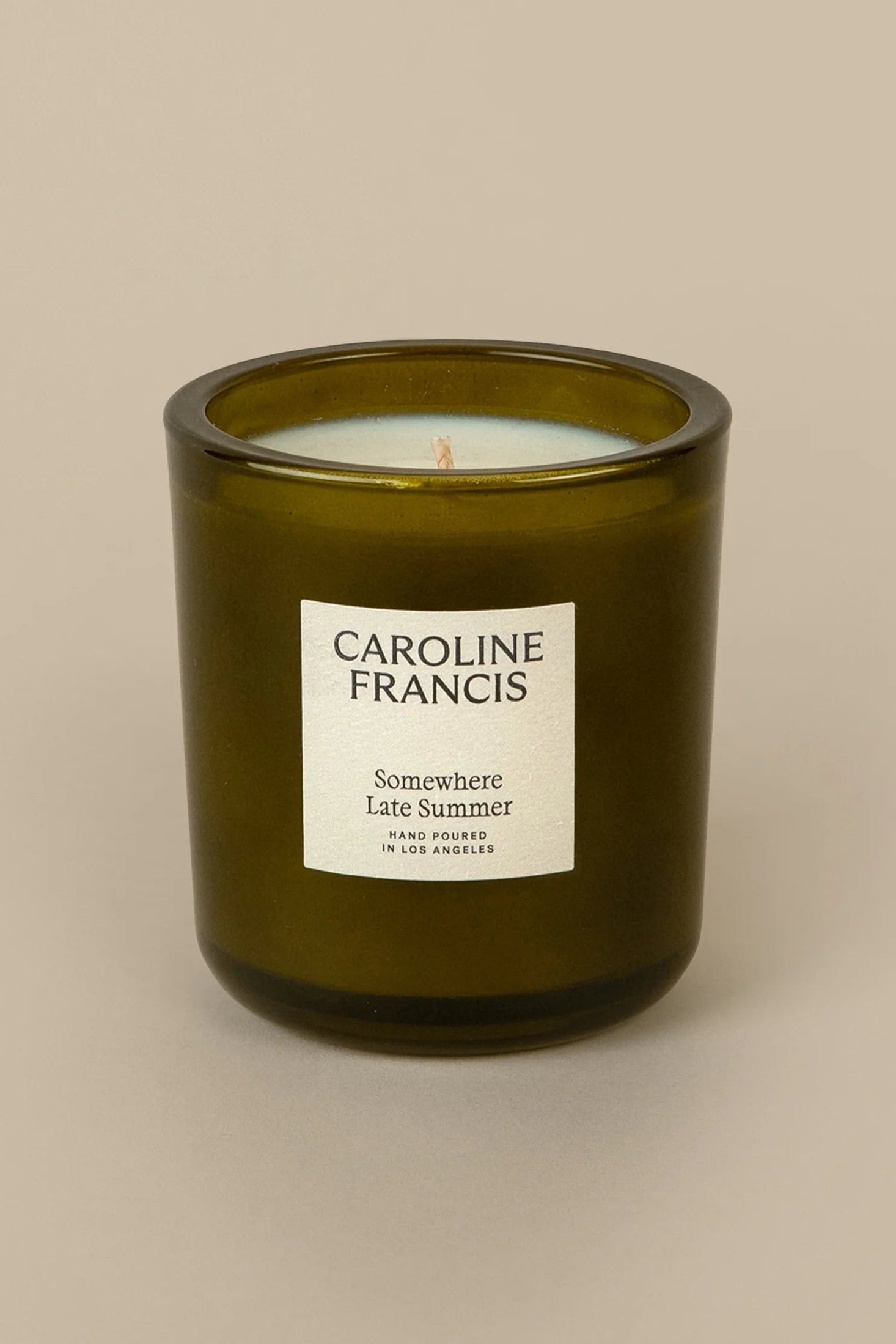 A green glass candle with a white label that reads 'CAROLINE FRANCIS' and 'Somewhere Late Summer'.