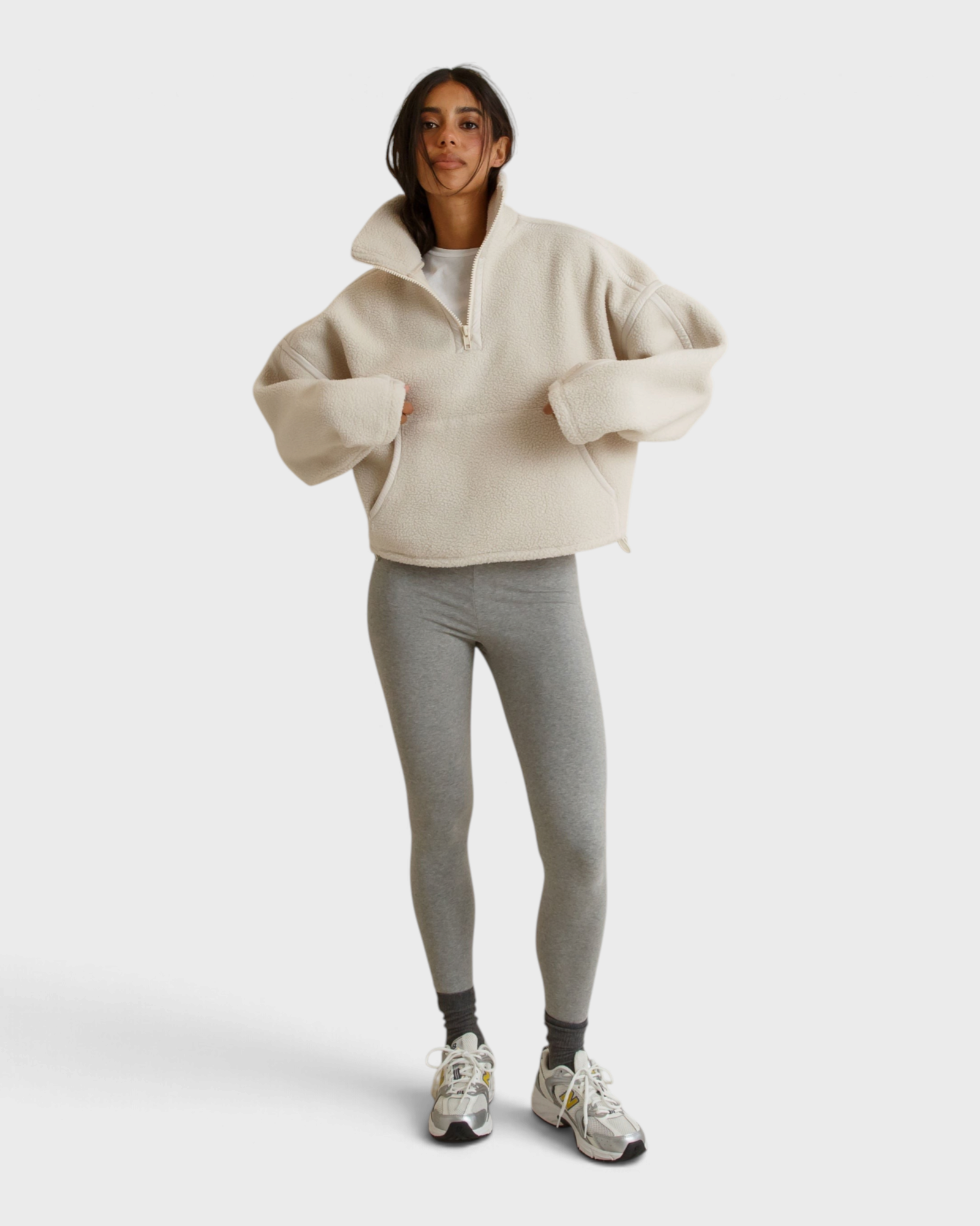 Model wearing JONES + CO Tristan sugar cream sherpa half-zip pullover with grey leggings and athletic sneakers